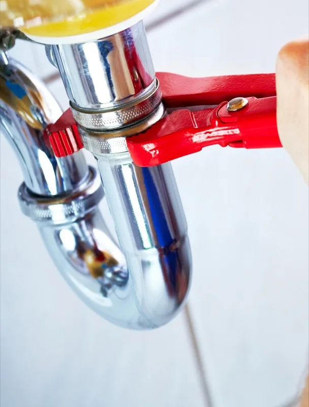 Plumber using a pipe wrench to repair a chrome P-trap